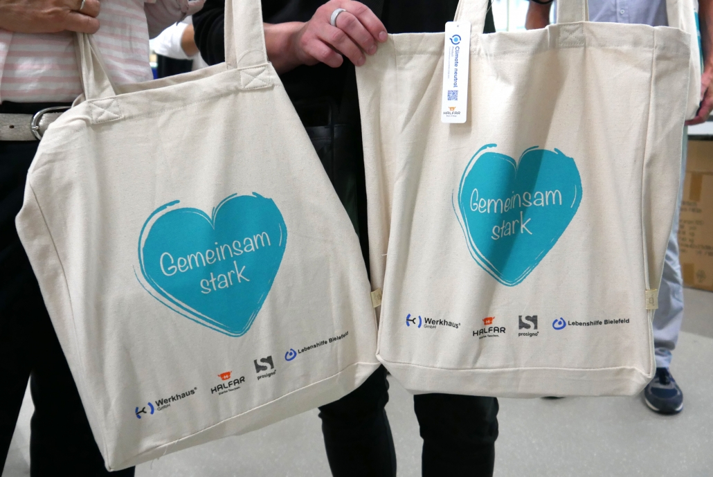 Two cotton bags printed with the Gemeinsam stark design and the logos of Werkhaus, Halfar, prosigno and Lebenshilfe Bielefeld.