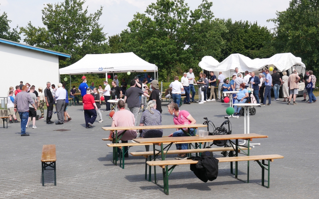 Guests gather outdoors around benches and tents during the Gemeinsam stark cooperation celebration.