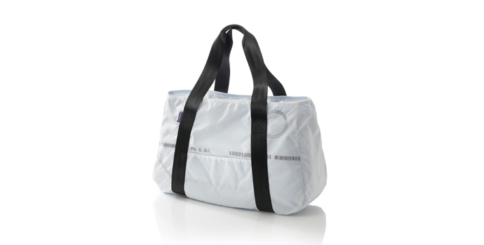 Weisse Tasche aus Airbag-Material mit schwarzen Henkeln vor hellem Hintergrund.