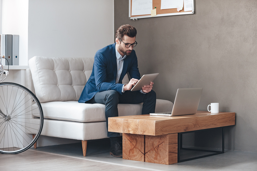 Mitarbeitender sitzt auf einem Sofa und arbeitet mit seinem Tablet