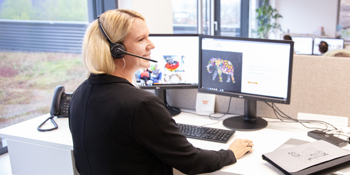 Mitarbeitende von HALFAR® mit Headset an einem Arbeitsplatz mit Stehtisch und moderner Ausstattung
