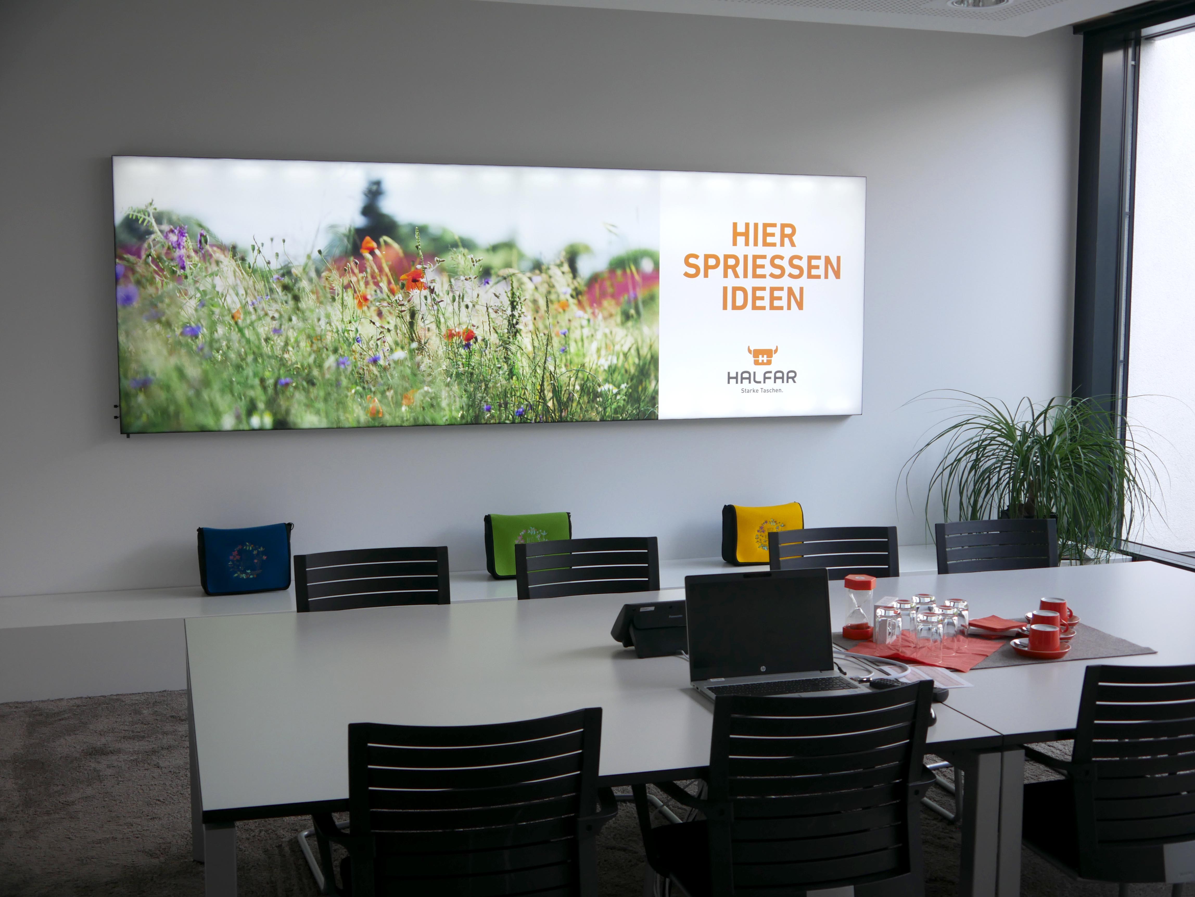 Besprechungsraum bei HALFAR® mit einem Banner das eine blühende Wiese zeigt und den Schriftzug "Hier spriessen Ideen"