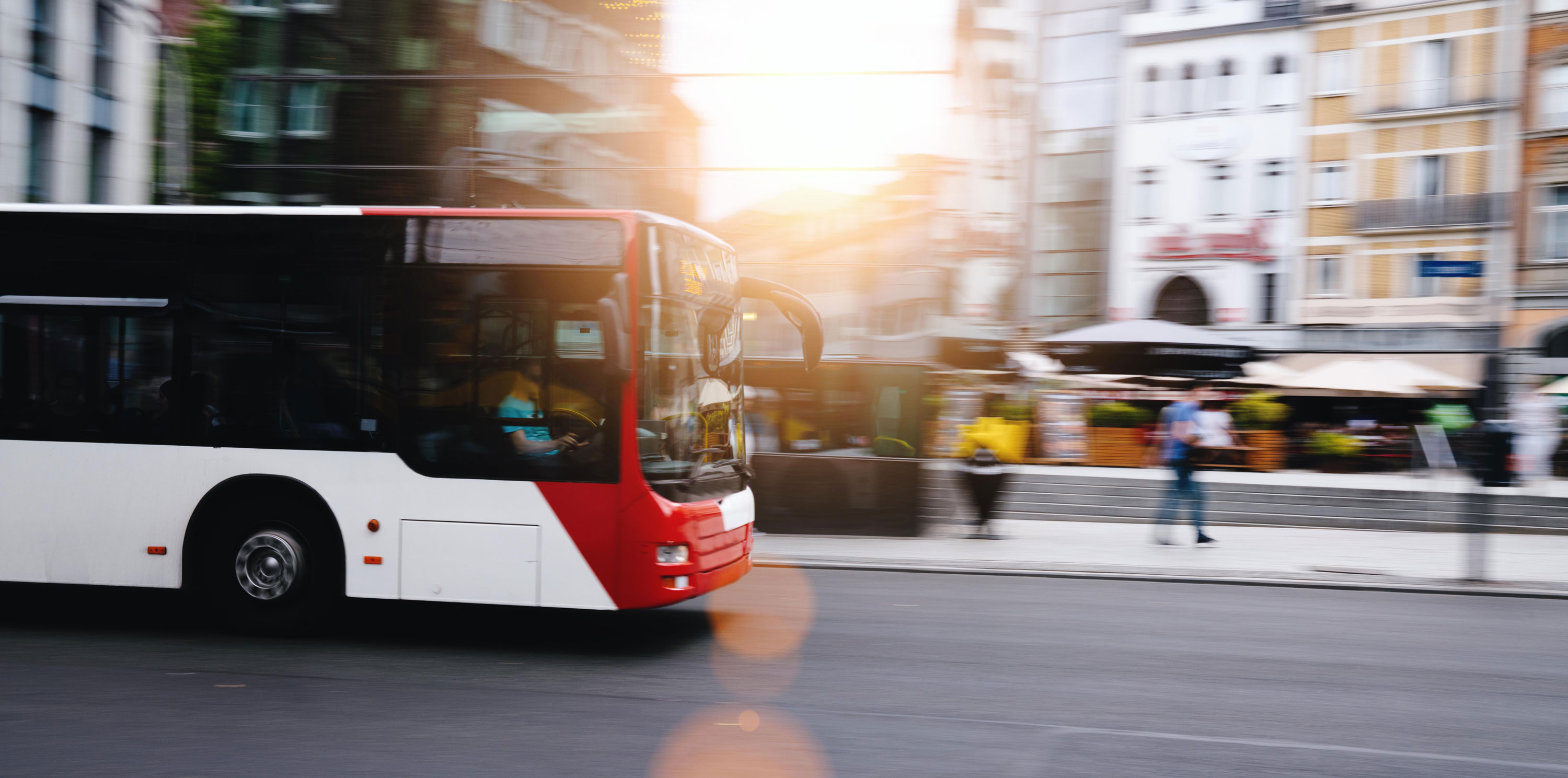 Ein Bus fährt über eine Straße, daneben Häuser und Fußgänger