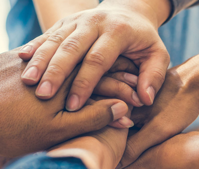 Mitarbeitende die im Kreis stehen und ihre Hände als Gäste der Gemeinschaft aufeinander legen