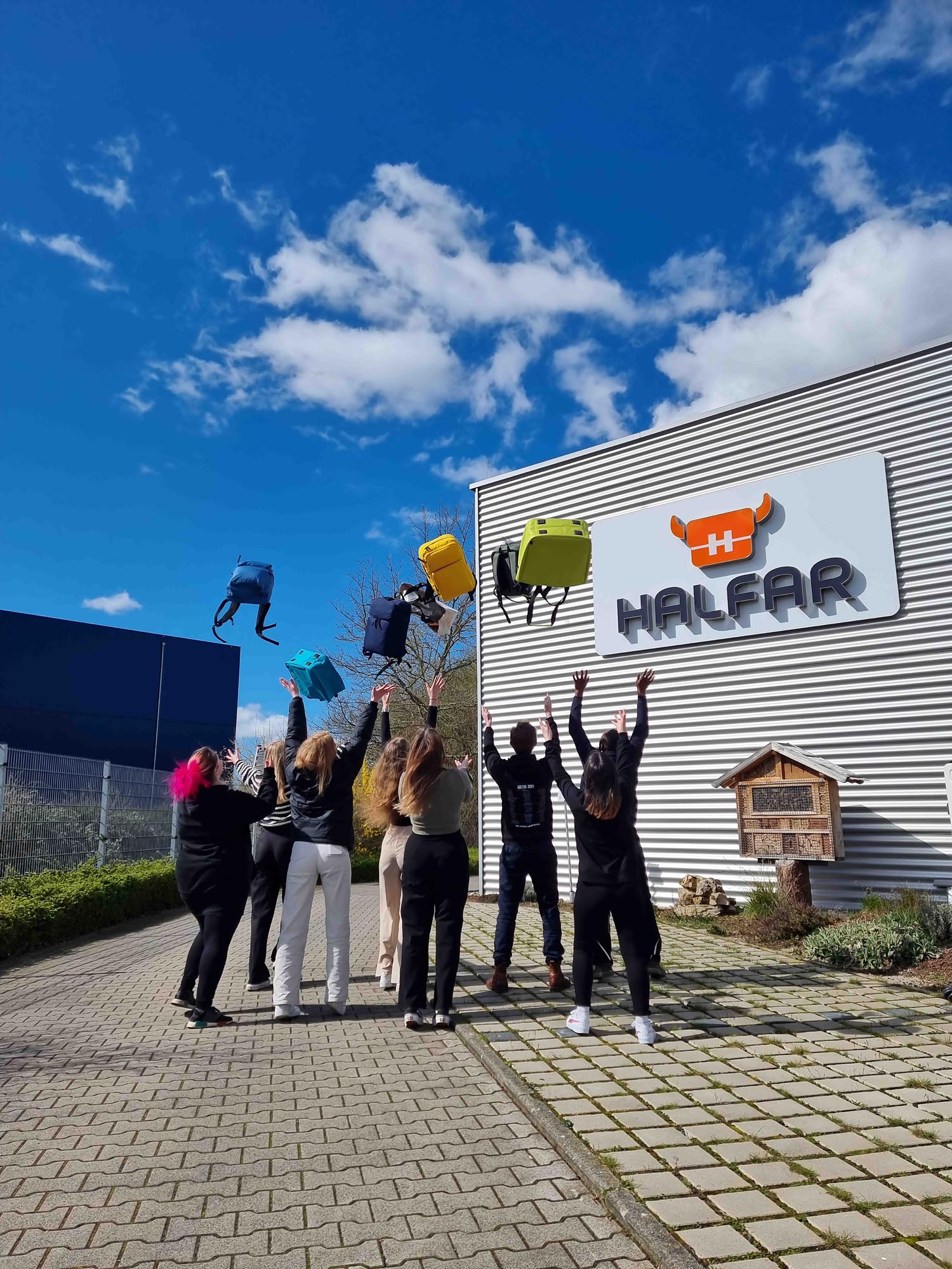 Auszubildende von Halfar werfen Taschen vor dem Firmengebäude in die Luft