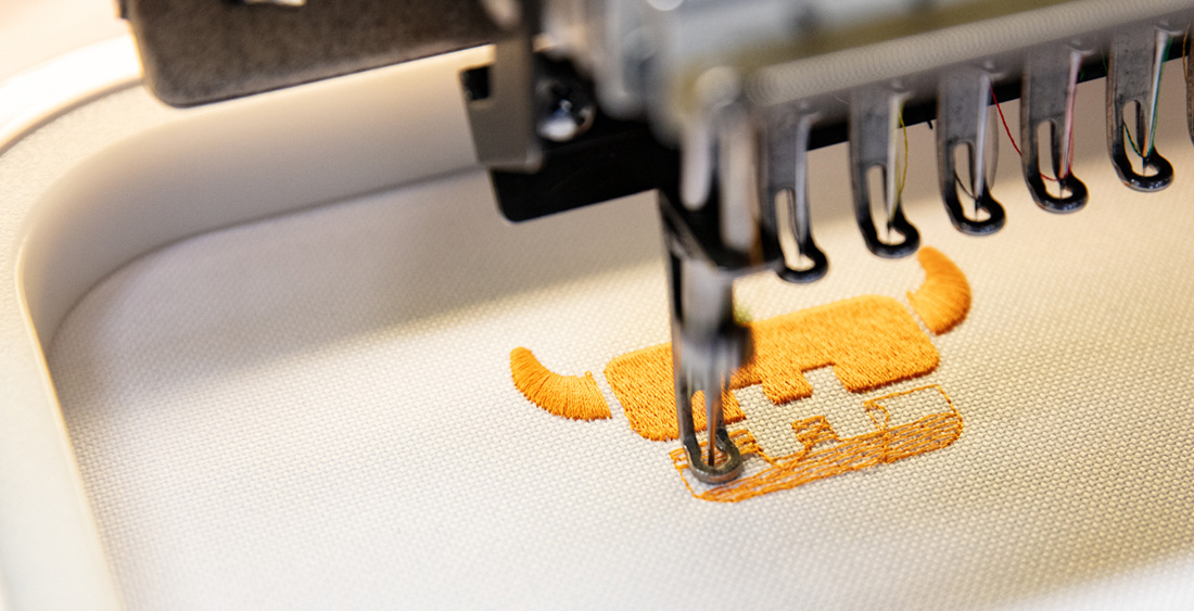 Stickmaschine stickt das HALFAR® Logo auf einen Werberucksack