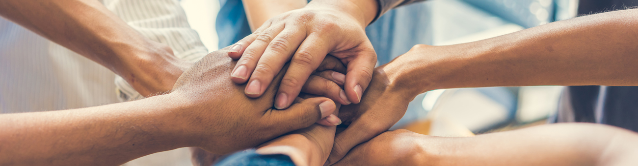 Mehrere Hände aufeinander als Zeichen für Zusammenhalt und Gemeinschaft